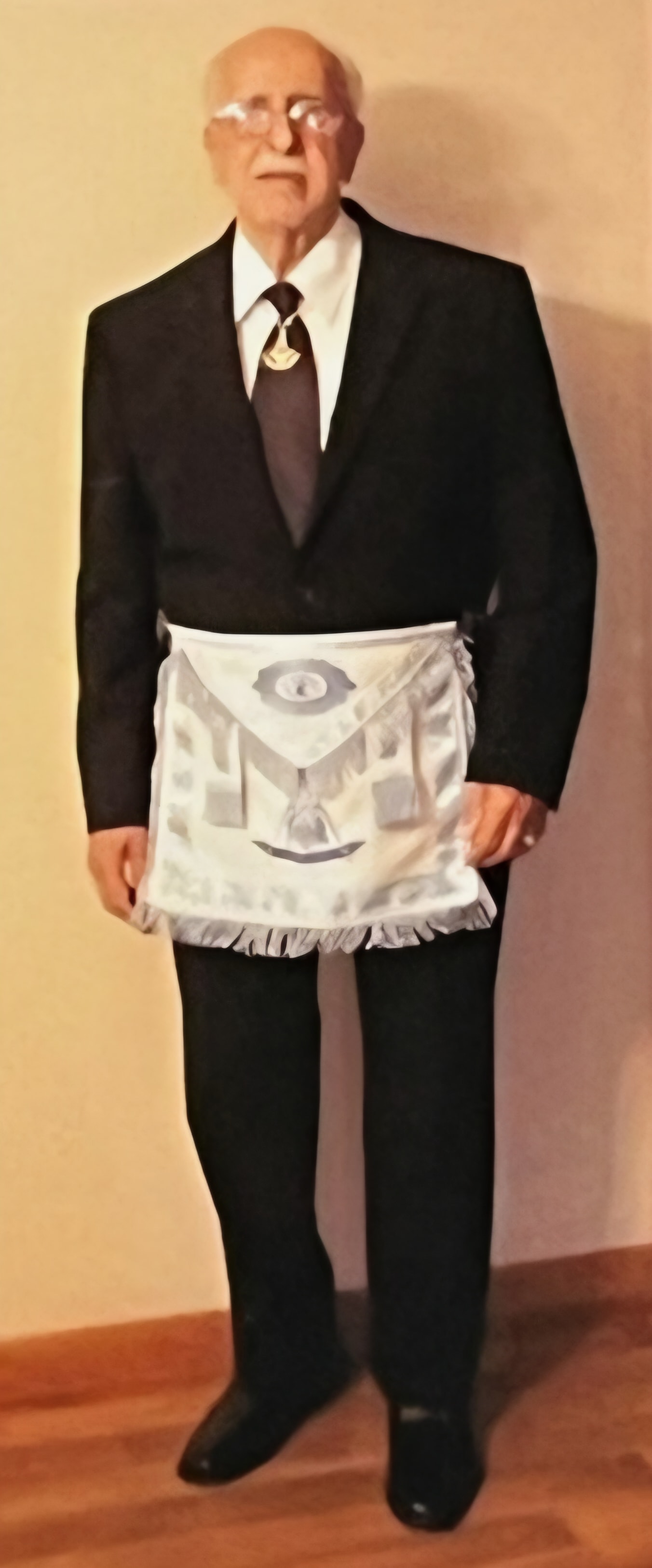 Brother standing in formal suit wearing a white Masonic apron with square and compass emblem