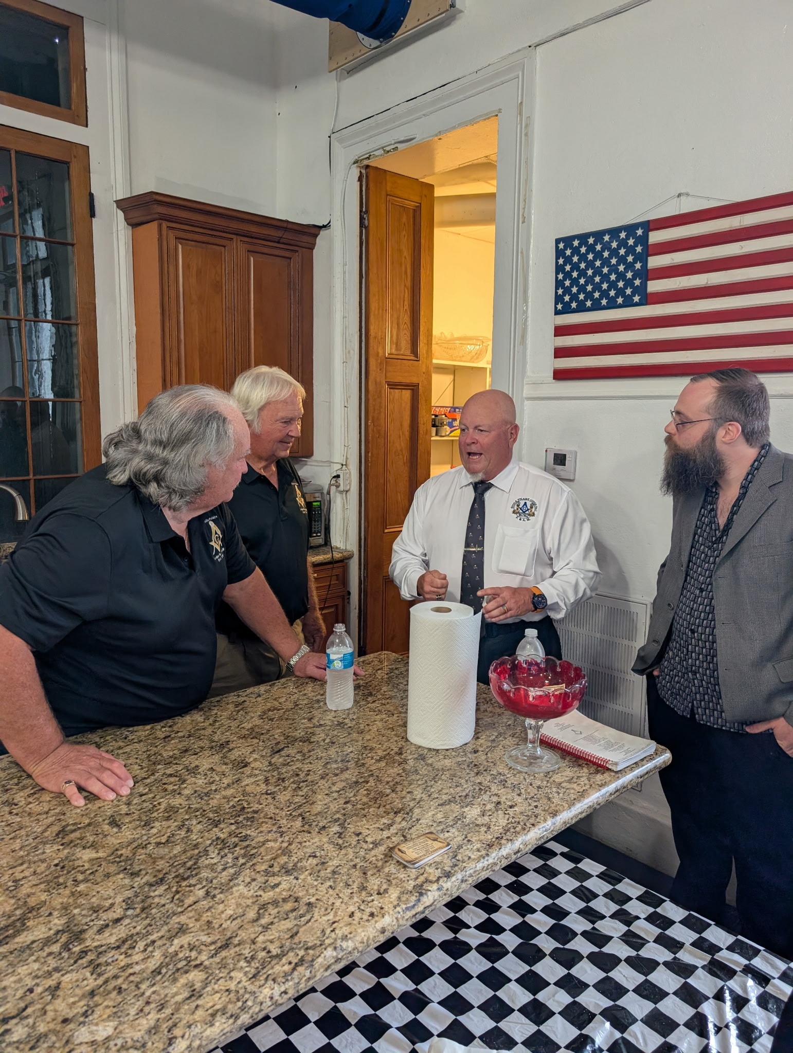 Four lodge brothers in conversation at the kitchen counter with an American flag on the wall