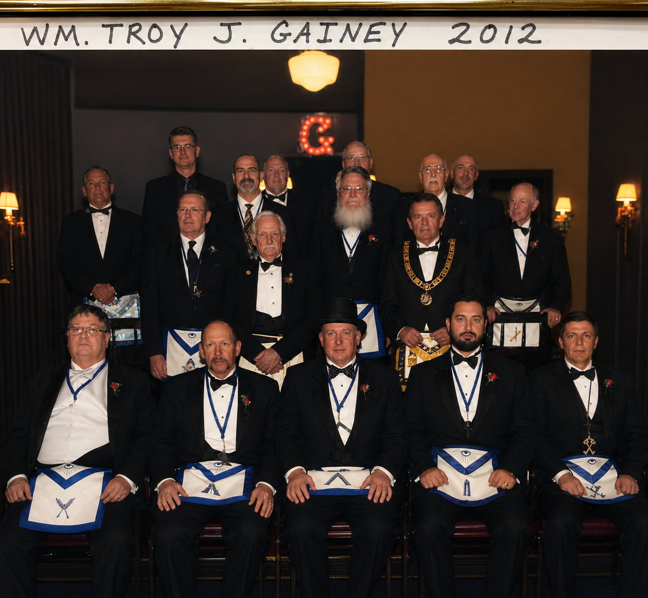 W.M. Troy J. Gainey 2012 — lodge officers in tuxedos and Masonic aprons posed in the lodge hall with the illuminated G symbol